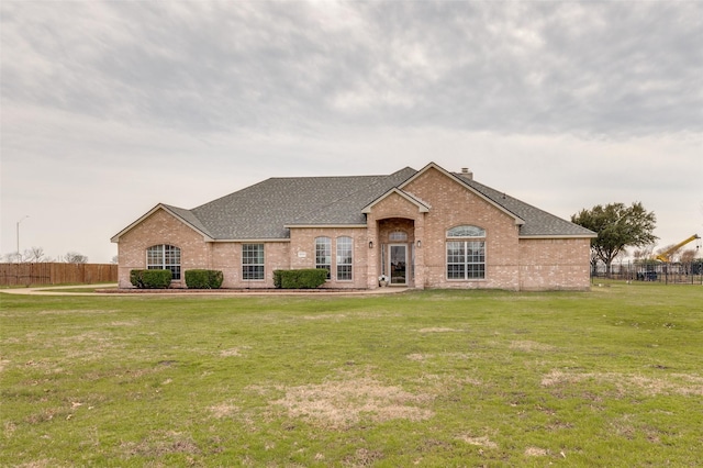 french country inspired facade with brick siding, fence, a front lawn, and roof with shingles