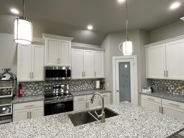 kitchen with light stone counters, appliances with stainless steel finishes, a sink, white cabinetry, and backsplash