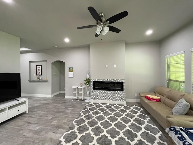 living area featuring arched walkways, baseboards, a tiled fireplace, and recessed lighting