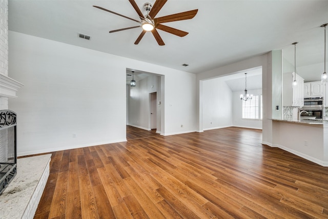 unfurnished living room with visible vents, a large fireplace, wood finished floors, baseboards, and ceiling fan with notable chandelier