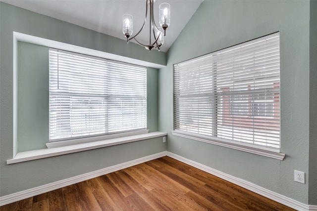 spare room featuring baseboards, a chandelier, vaulted ceiling, and wood finished floors