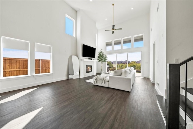 living area featuring dark wood-style floors, stairs, baseboards, and a glass covered fireplace