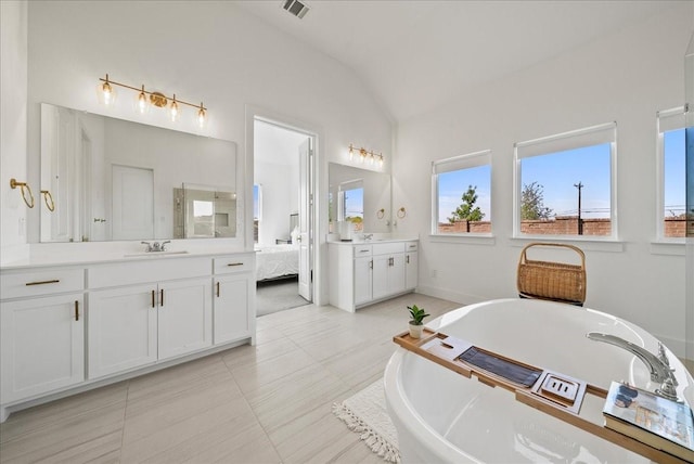 ensuite bathroom featuring two vanities, visible vents, vaulted ceiling, a sink, and a freestanding tub