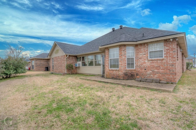 rear view of property featuring a shingled roof, cooling unit, brick siding, and a yard