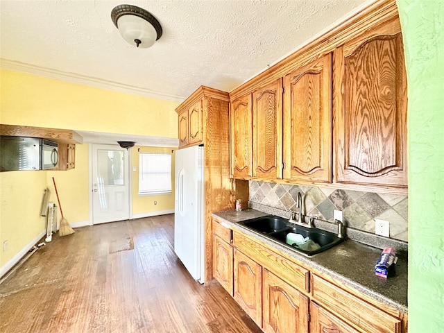 kitchen featuring black microwave, a sink, freestanding refrigerator, decorative backsplash, and dark wood-style floors