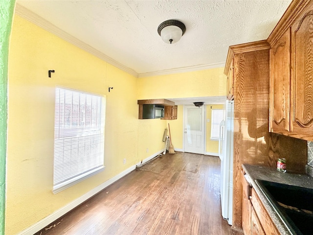 kitchen featuring dark wood-style flooring, crown molding, brown cabinetry, freestanding refrigerator, and a textured ceiling