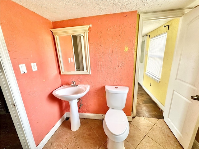 half bathroom with a textured wall, a textured ceiling, toilet, and tile patterned floors