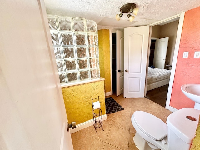 bathroom featuring a textured ceiling, baseboards, toilet, and tile patterned floors