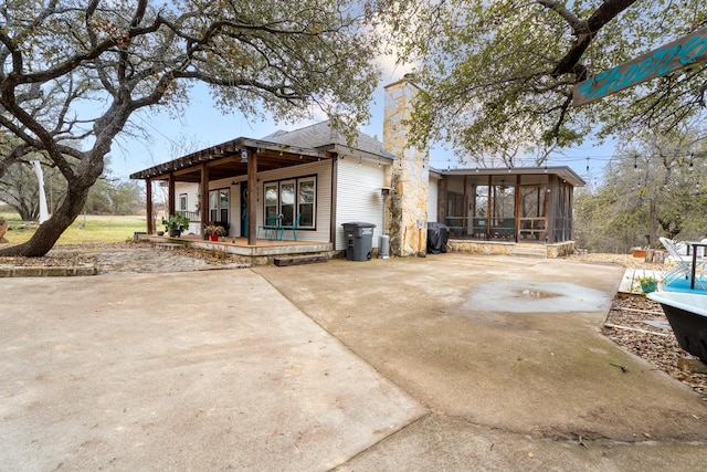 rear view of property with a sunroom, a patio area, and a chimney