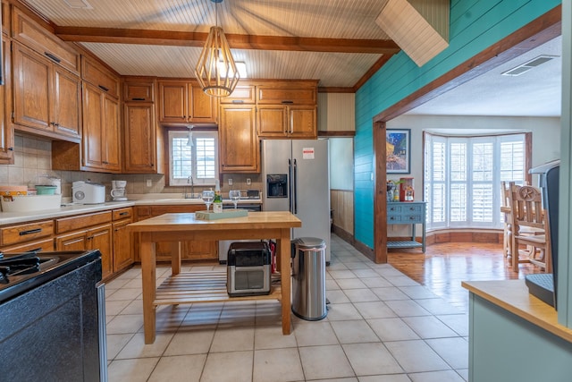 kitchen featuring visible vents, brown cabinetry, beam ceiling, and stainless steel fridge with ice dispenser