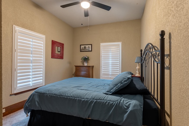 carpeted bedroom with a textured wall, baseboards, and ceiling fan