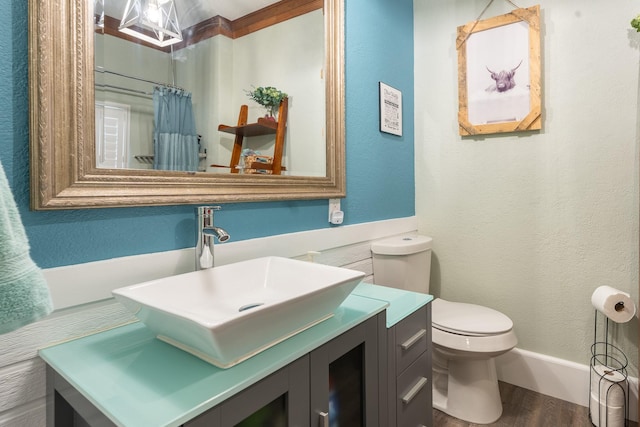 bathroom with a textured wall, curtained shower, toilet, wood finished floors, and vanity