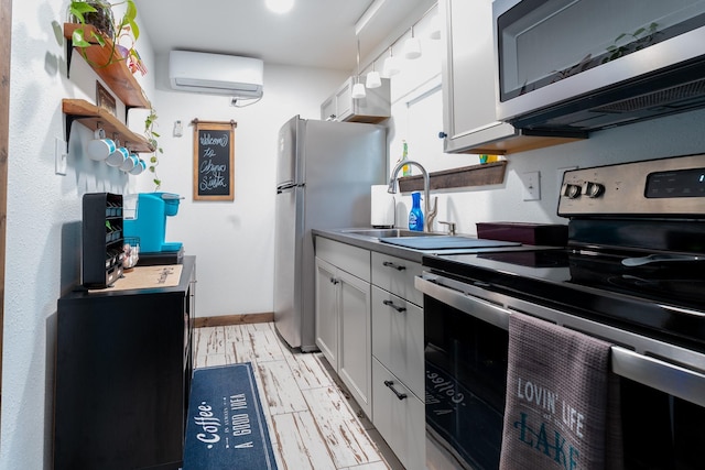 kitchen with wood finish floors, a wall unit AC, appliances with stainless steel finishes, white cabinets, and a sink