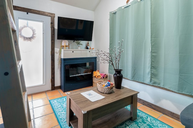 tiled living area with a wealth of natural light, a glass covered fireplace, vaulted ceiling, and baseboards