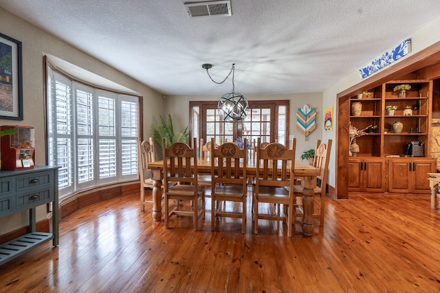 dining room featuring visible vents, baseboards, a textured ceiling, light wood-style floors, and a notable chandelier