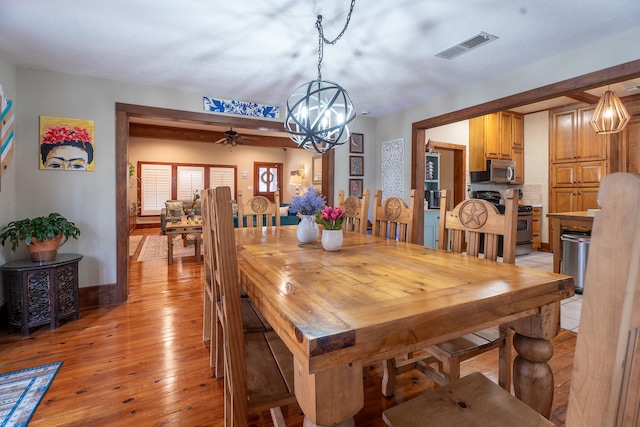 dining room with light wood-style flooring, visible vents, baseboards, and ceiling fan with notable chandelier