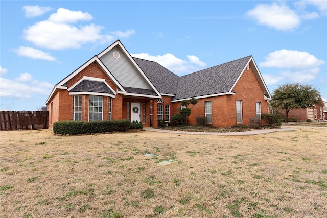 view of front of property with brick siding, roof with shingles, a front yard, and fence