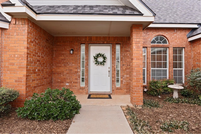 view of exterior entry featuring brick siding and roof with shingles