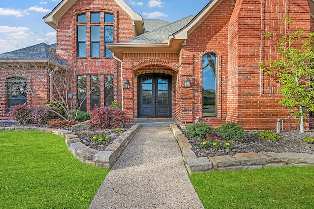 property entrance featuring brick siding, a shingled roof, a yard, and french doors