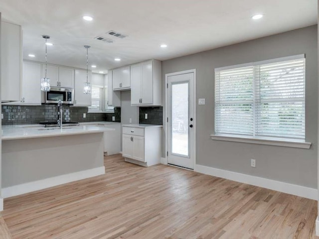 kitchen featuring light countertops, stainless steel microwave, white cabinets, and decorative backsplash