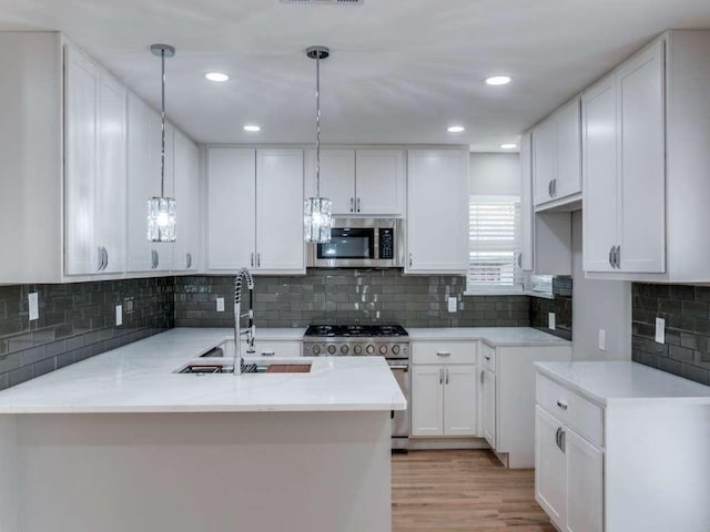 kitchen featuring decorative light fixtures, a sink, a peninsula, stainless steel appliances, and white cabinetry