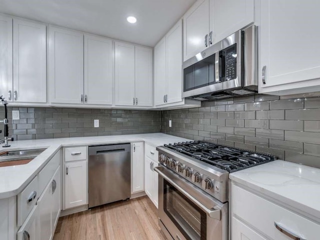 kitchen featuring decorative backsplash, white cabinets, light wood-style flooring, appliances with stainless steel finishes, and a sink