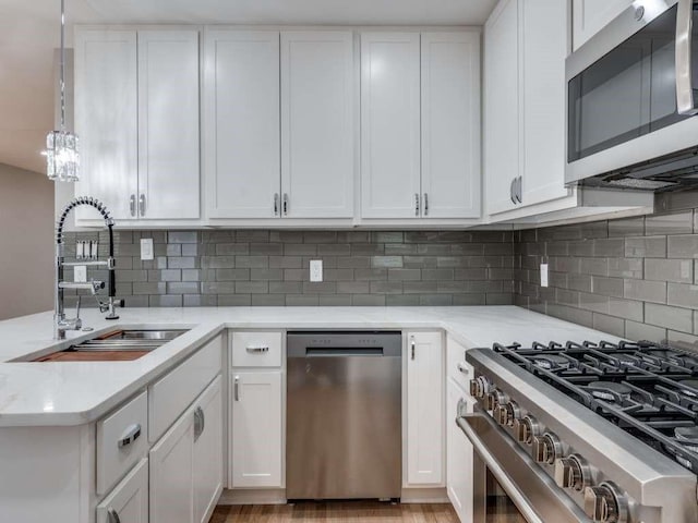 kitchen featuring hanging light fixtures, decorative backsplash, appliances with stainless steel finishes, white cabinetry, and a sink