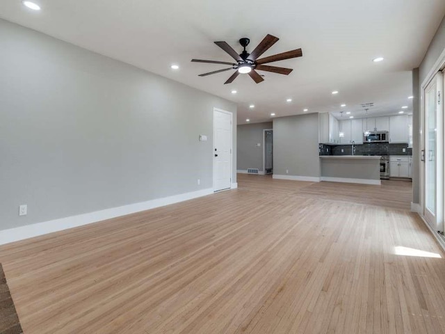 unfurnished living room featuring ceiling fan, recessed lighting, a sink, baseboards, and light wood-type flooring