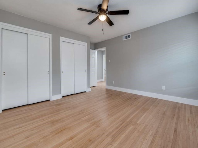 unfurnished bedroom featuring baseboards, visible vents, light wood-style flooring, ceiling fan, and multiple closets