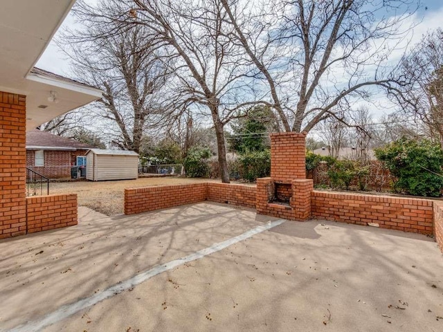 view of patio featuring a storage shed, a fireplace, fence, and an outbuilding