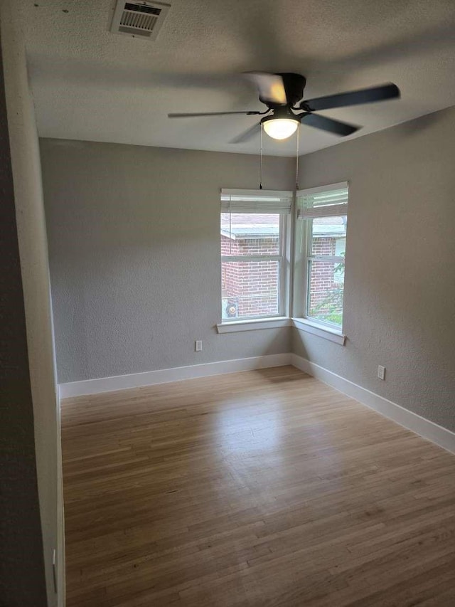 empty room with ceiling fan, a textured wall, baseboards, wood finished floors, and visible vents