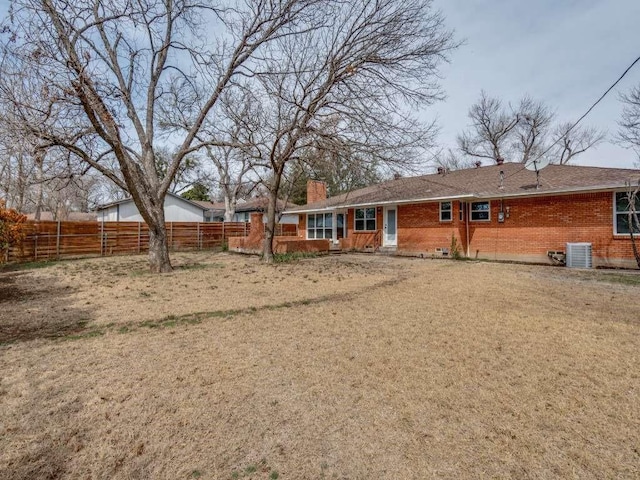 rear view of property with brick siding, a chimney, a lawn, central AC, and fence