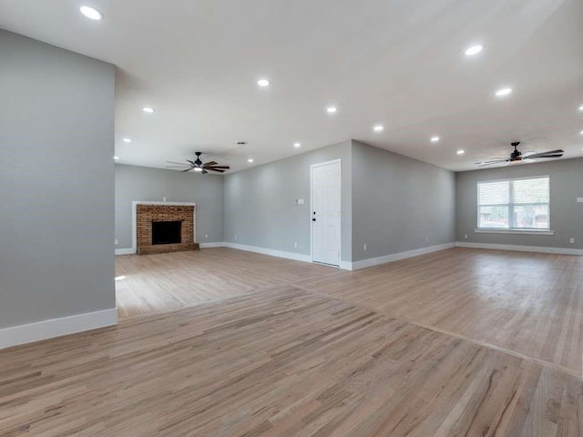 unfurnished living room with baseboards, light wood-style flooring, ceiling fan, a brick fireplace, and recessed lighting