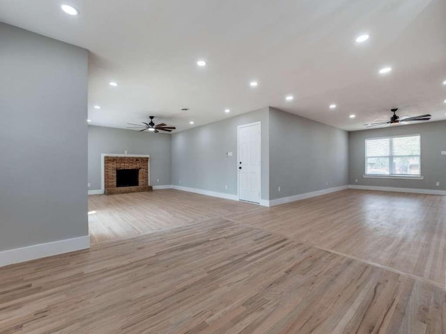 unfurnished living room featuring a brick fireplace, a ceiling fan, baseboards, and light wood-type flooring