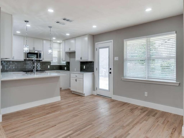 kitchen featuring backsplash, baseboards, white cabinets, stainless steel microwave, and light wood-style flooring