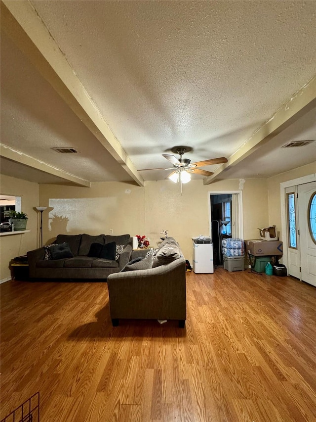 living room featuring a textured ceiling, beamed ceiling, wood finished floors, and visible vents