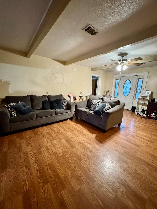 living area with beam ceiling, visible vents, a textured ceiling, and wood finished floors