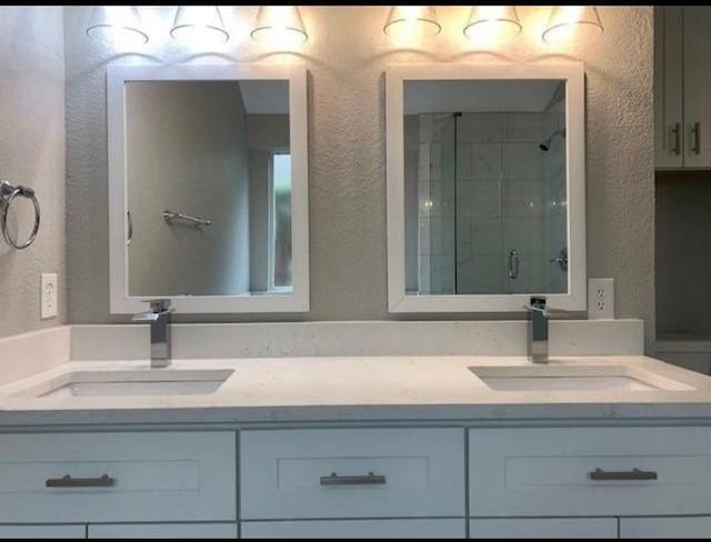 bathroom with double vanity, a stall shower, a sink, and a textured wall