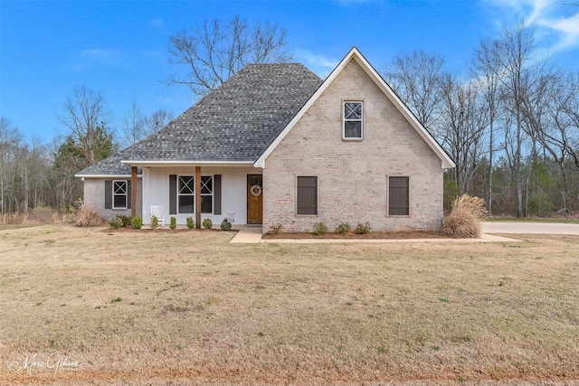 view of front of home with a front yard, brick siding, and roof with shingles