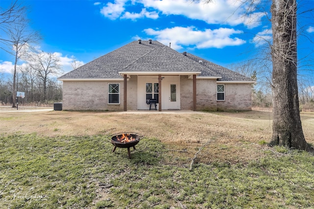 rear view of property with a patio, an outdoor fire pit, a shingled roof, brick siding, and a yard