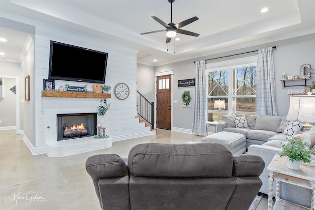 living area with baseboards, ceiling fan, a fireplace, a tray ceiling, and recessed lighting