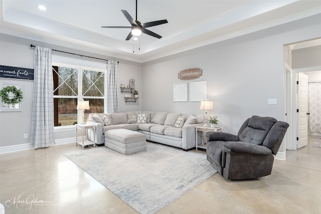 living room featuring a tray ceiling, concrete floors, ceiling fan, and ornamental molding