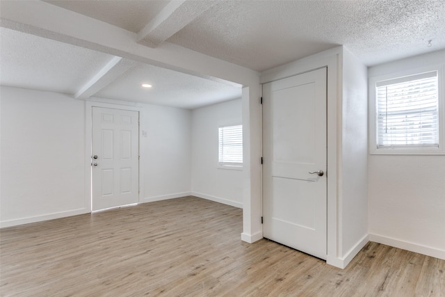 empty room featuring light wood-style flooring, baseboards, a textured ceiling, and beamed ceiling