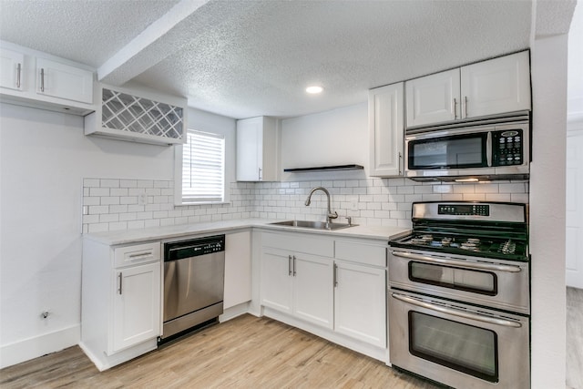 kitchen with white cabinets, stainless steel appliances, light countertops, light wood-style floors, and a sink