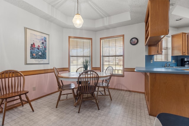 dining space featuring a textured ceiling, light floors, a raised ceiling, and a healthy amount of sunlight