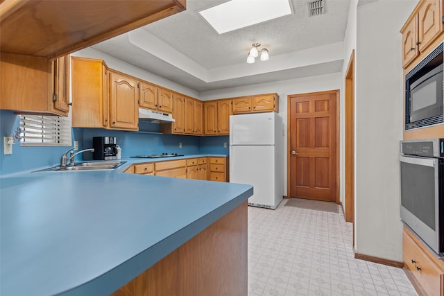 kitchen with light floors, freestanding refrigerator, stainless steel oven, a sink, and under cabinet range hood