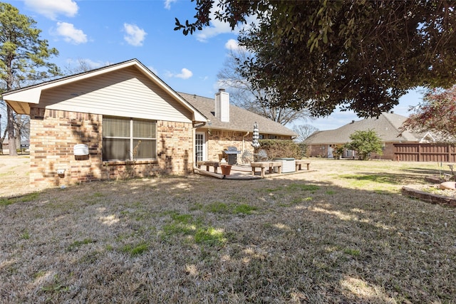 rear view of property featuring brick siding, a patio, a chimney, a lawn, and fence