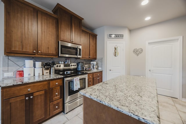 kitchen with light tile patterned flooring, backsplash, appliances with stainless steel finishes, and light stone countertops