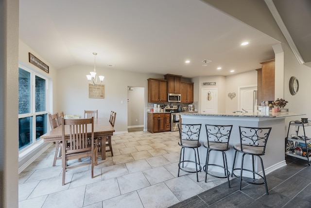 kitchen featuring a breakfast bar area, light stone counters, a peninsula, an inviting chandelier, and stainless steel appliances