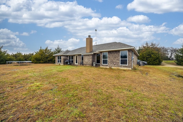 back of house featuring brick siding, a lawn, a chimney, and a trampoline